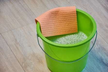 Groene emmer met sop en oranje doek op houten vloer